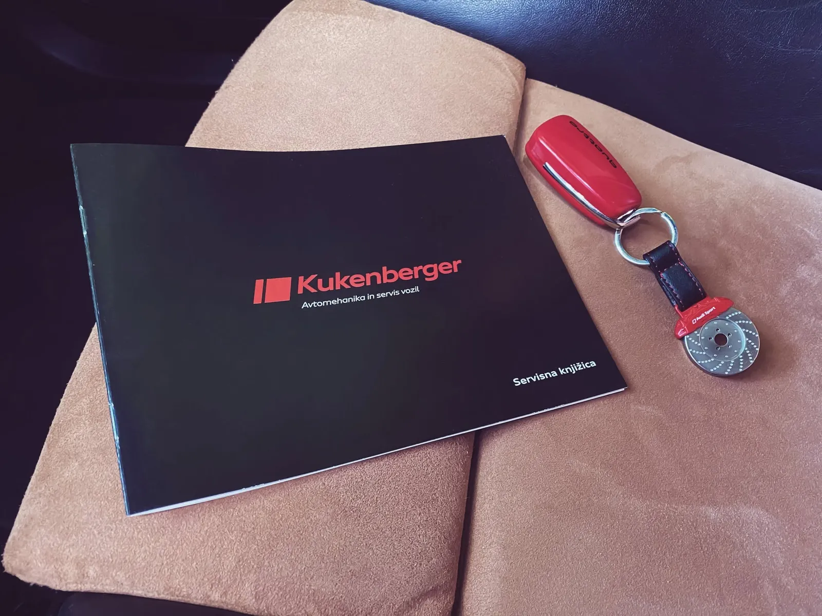 Kukenberger auto-service booklet mockup, black cover with red logo beside a red car key
