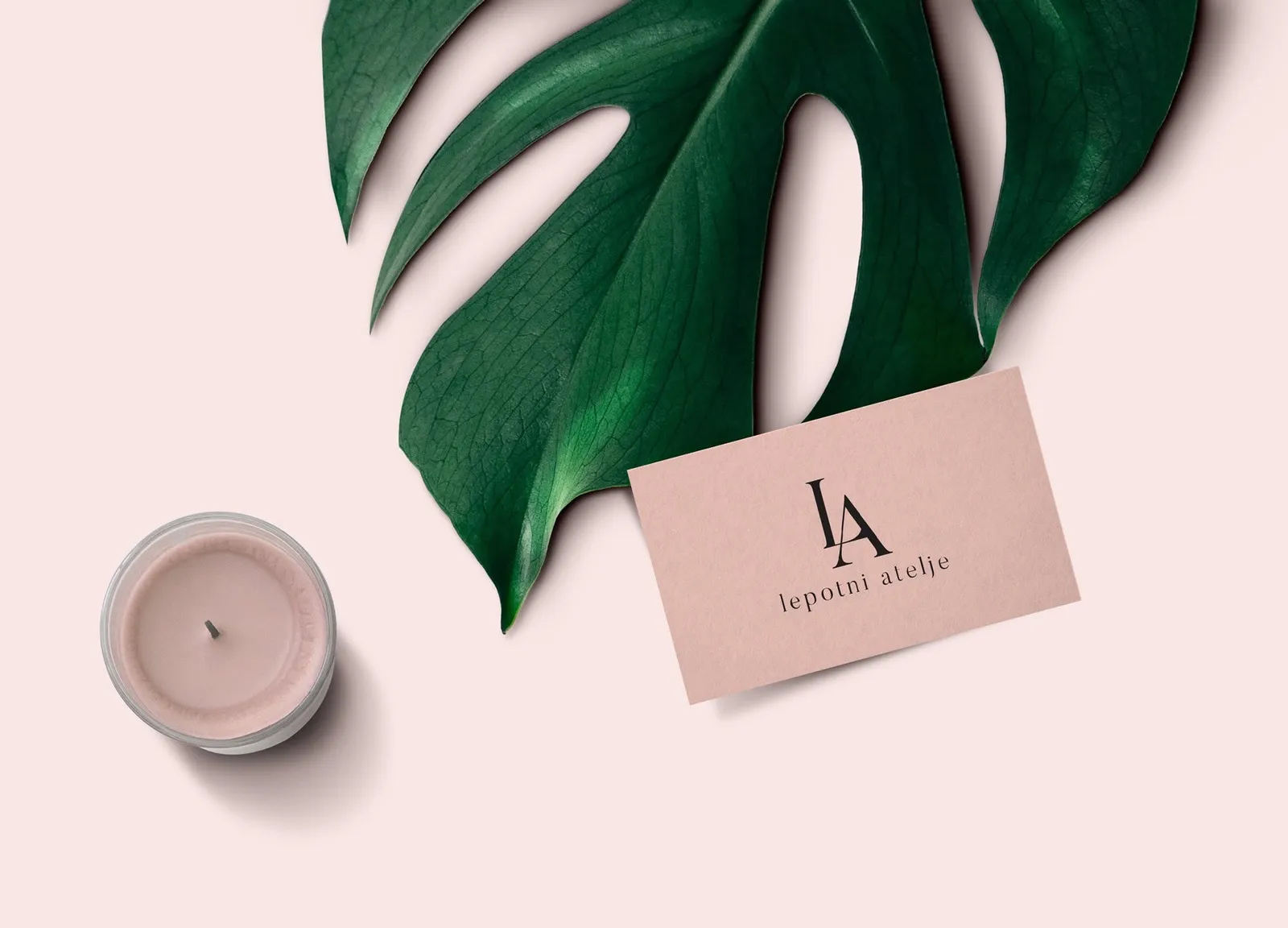 Lepotni Atelje business card mockup on blush pink with a dark monstera leaf and candle